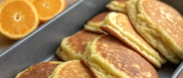 Stack of golden brown Mexican pancakes with butter melting on top and fresh strawberries on a white plate