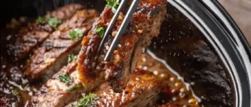 Sliced slow cooker beef brisket on a wooden cutting board, surrounded by roasted carrots and a small bowl of dark braising sauce, with a rustic linen napkin to the side.