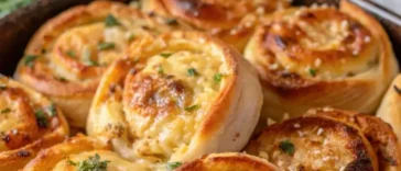 A close-up overhead shot of small garlic rolls made from rolled sandwich crusts, arranged in a round cast iron skillet, brushed with glistening garlic herb butter and sprinkled with coarse salt and chopped parsley, resting on a dark wooden table.
