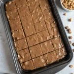 Broken pieces of Oklahoma Nut Candy on parchment paper, caramel-brown and crumbly with visible pecan chunks, photographed from above in warm natural light on a wood surface.